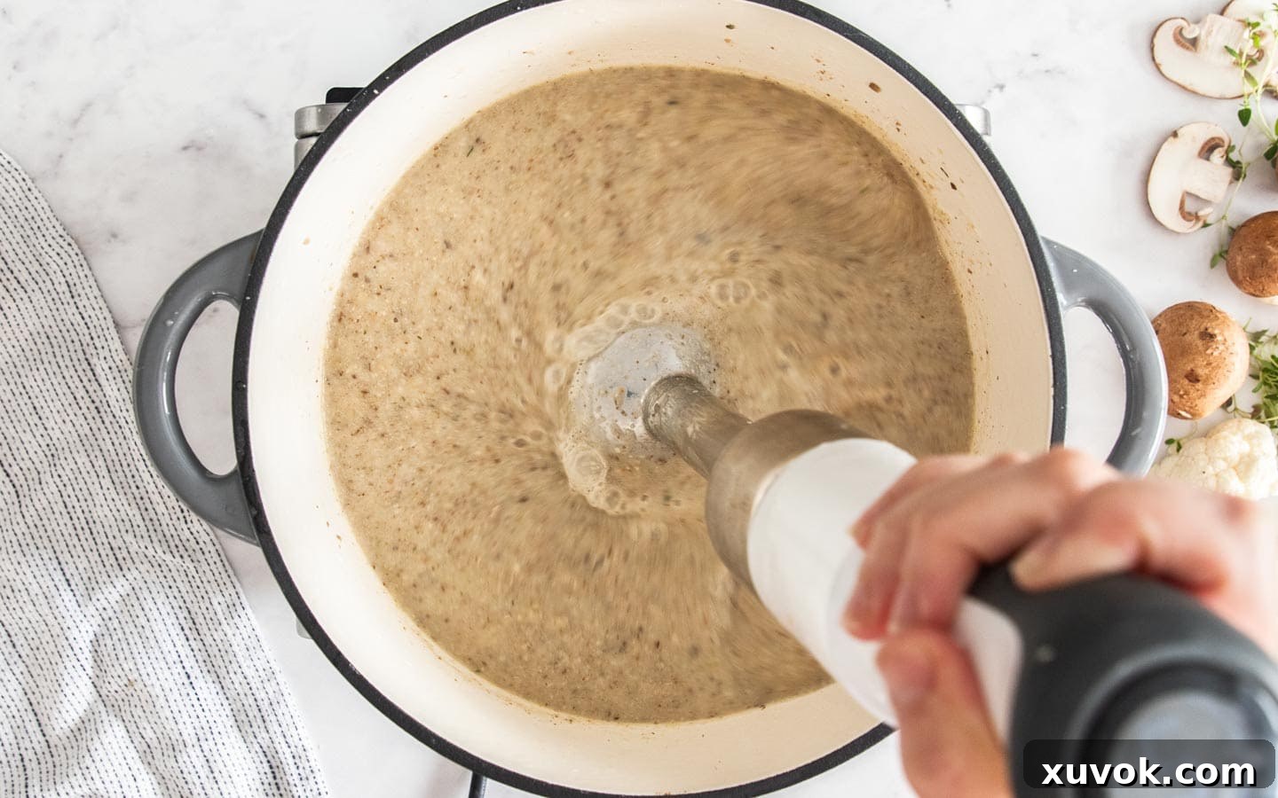 An immersion blender actively blending the mushroom cauliflower soup directly in the pot to a smooth consistency.