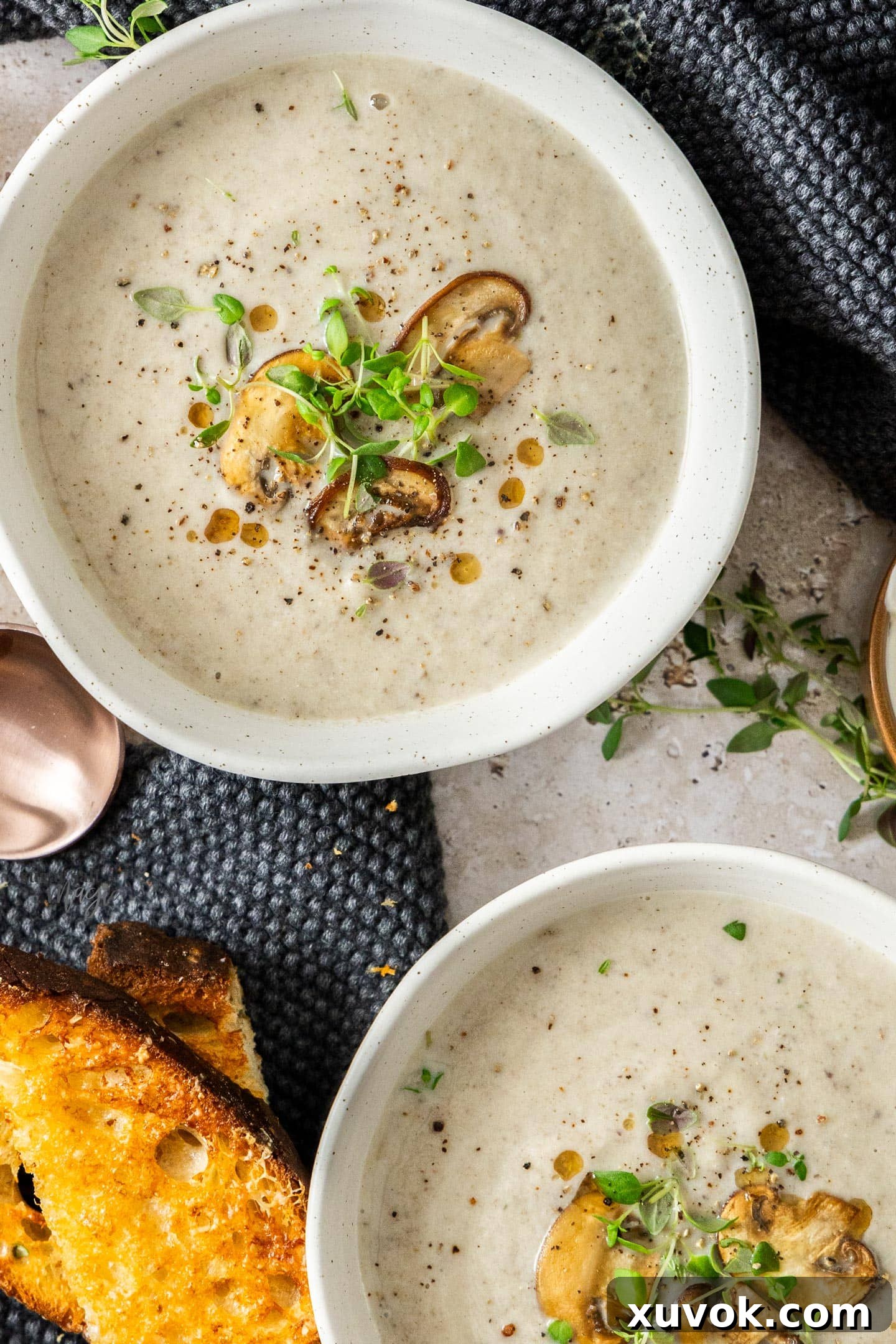 Top-down view of two beautifully garnished bowls of creamy mushroom cauliflower soup, topped with sautéed mushrooms and fresh thyme.