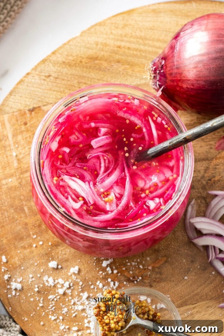 Bright pink pickled onions in a glass jar on a wooden board, a tangy condiment.