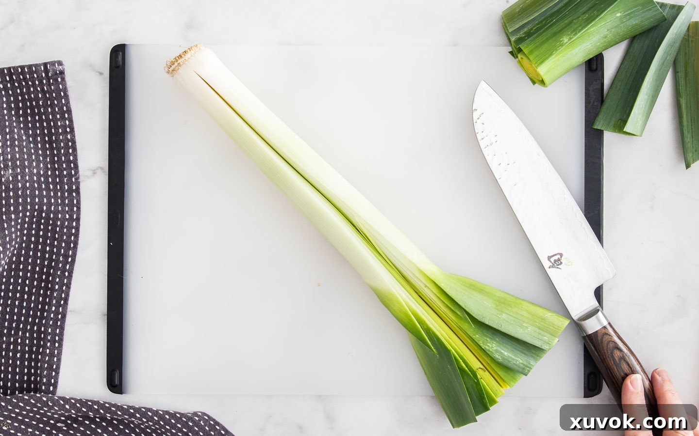A leek sliced half way through down the middle on a chopping board, demonstrating the initial cut for cleaning, maintaining root integrity.