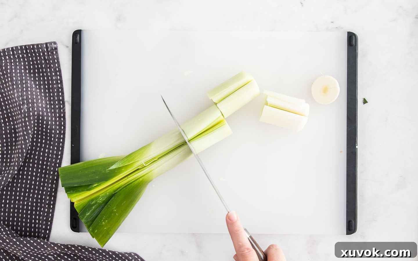 A leek being cut into 3 inch pieces after thorough cleaning, ready for roasting or braising.