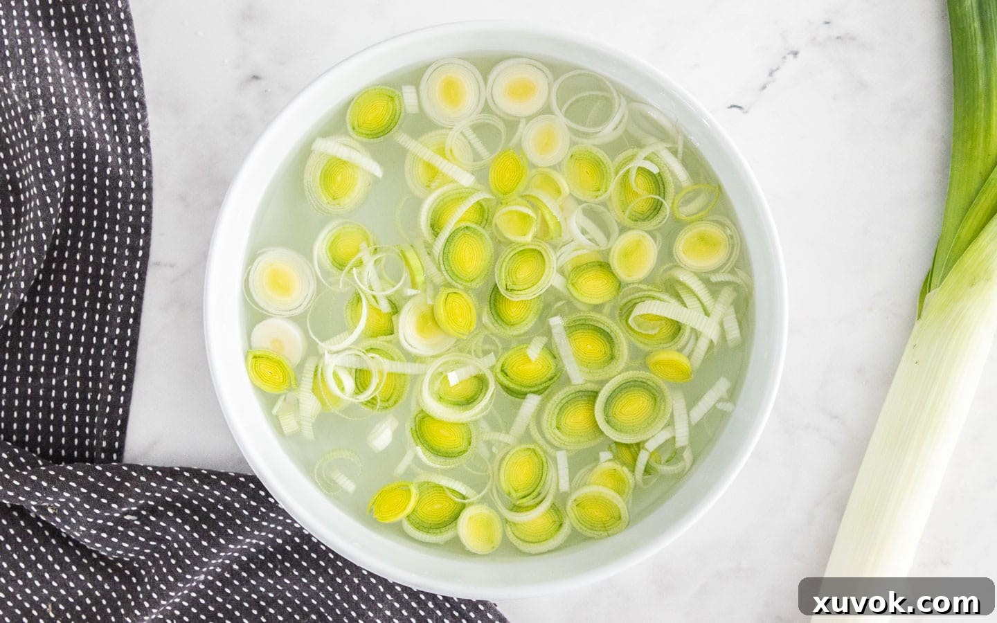 Rings of leek submerged in a bowl of cold water, being gently agitated to release dirt particles.