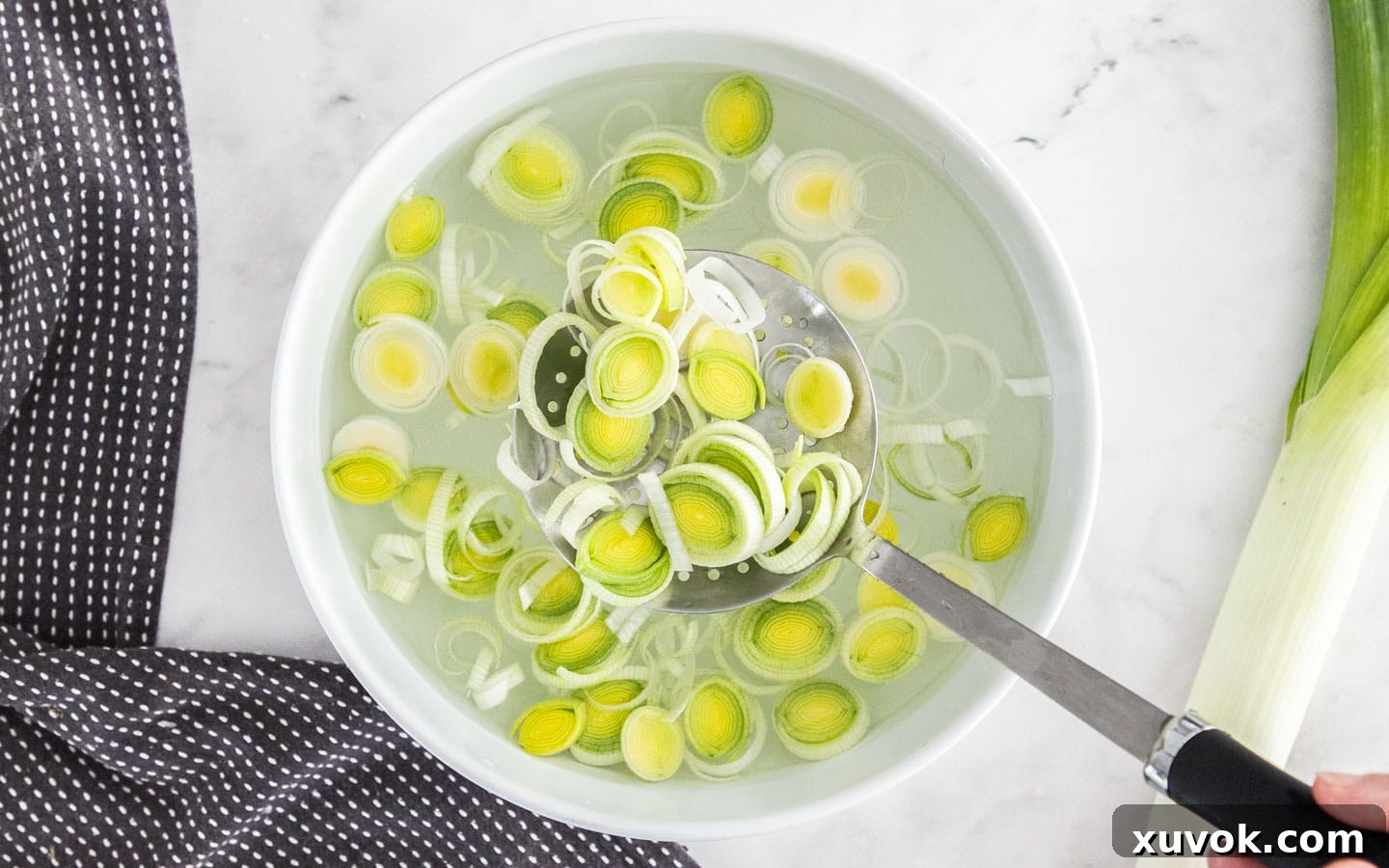Rings of leek being scooped out of water with a slotted spoon onto a kitchen towel for drying, avoiding re-contamination.