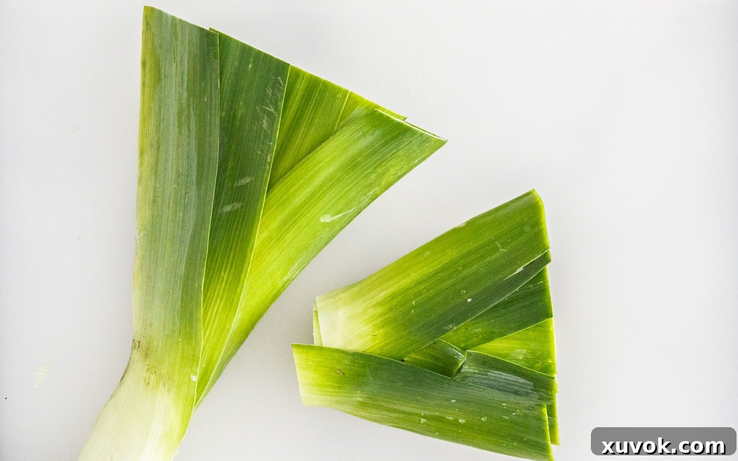 The top dark green leaves of two leeks, neatly trimmed and ready to be repurposed instead of discarded, showcasing a commitment to zero-waste cooking.