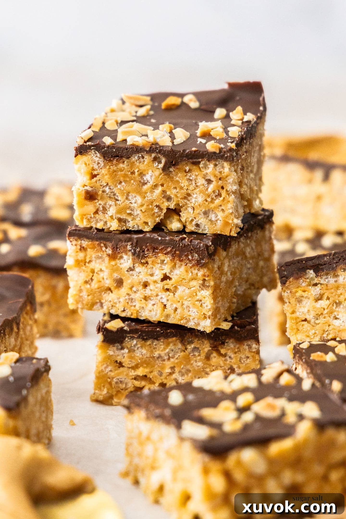 A stack of three neatly cut chocolate peanut butter rice krispie treats, showing the layers of chocolate and peanut butter crispy base.