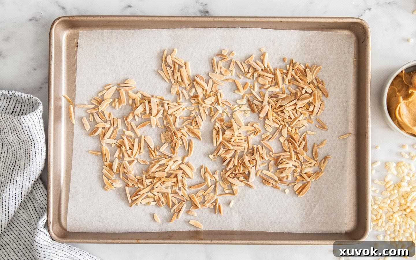 Golden toasted almonds spread on a baking sheet, ready to be added to the rice crispy mixture.