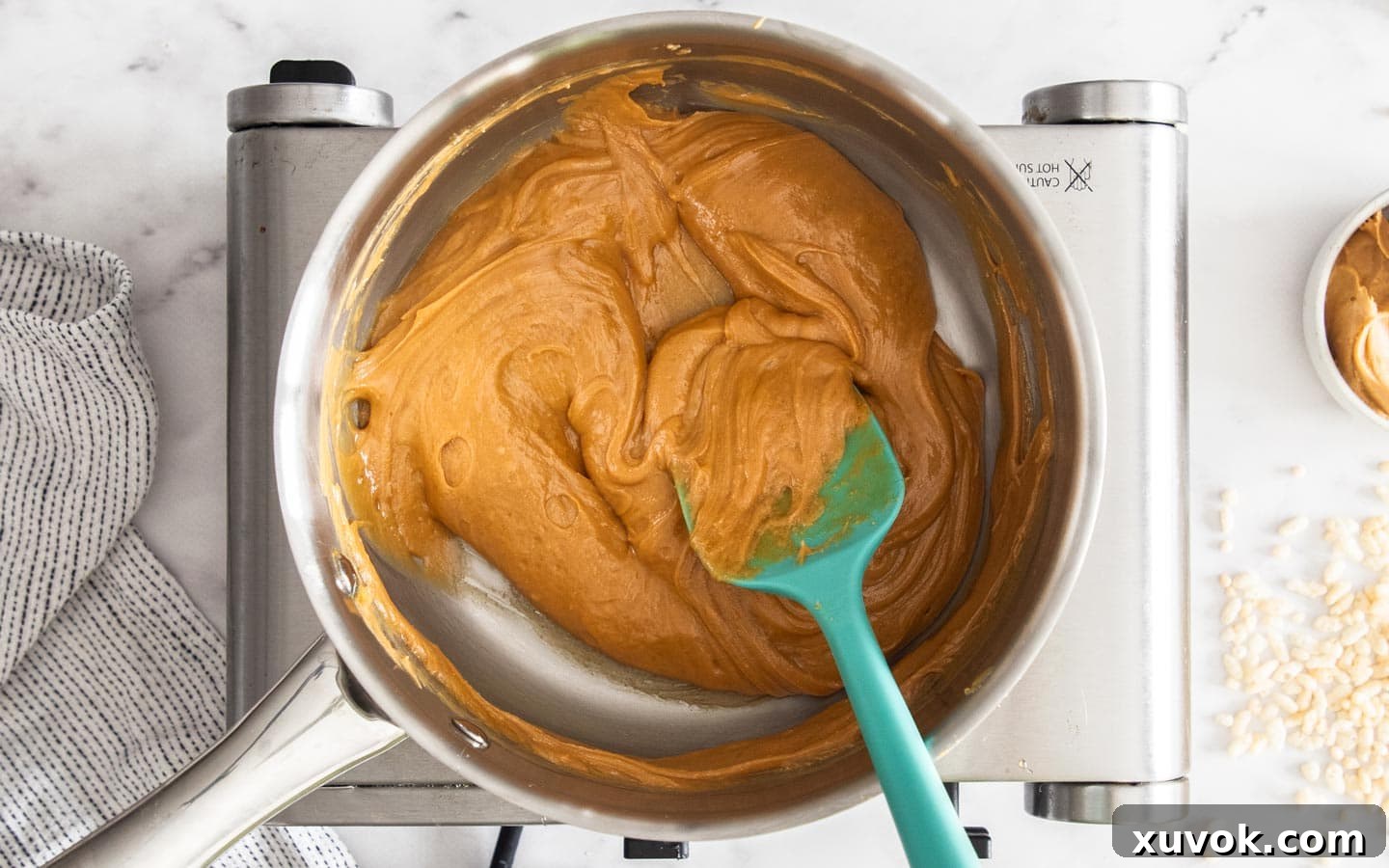 A saucepan filled with the melted peanut butter, syrup, and salt mixture, smooth and ready to be combined with the cereal.