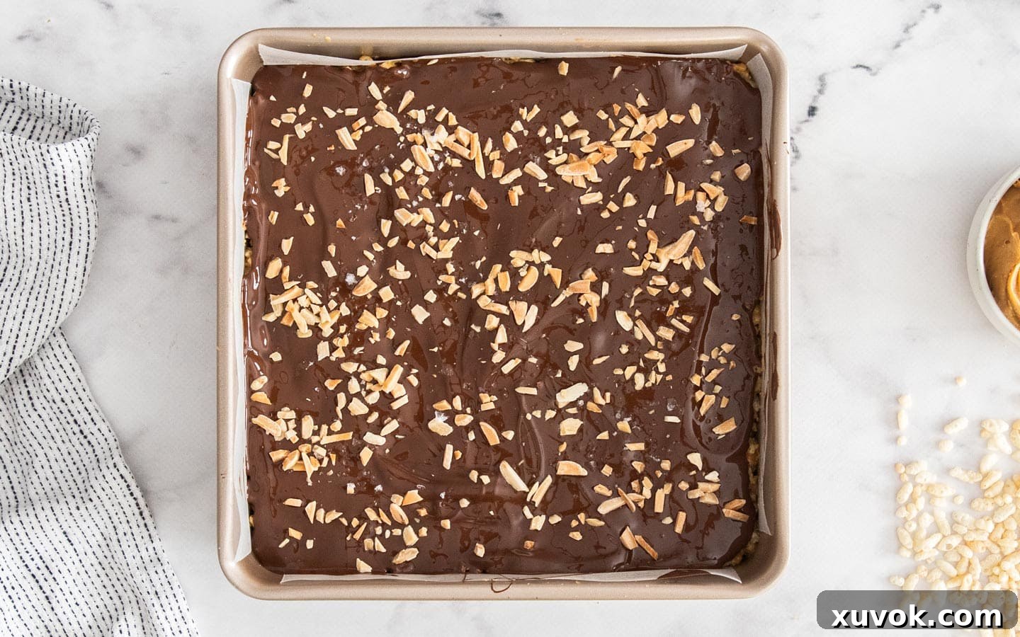 The pan of rice crispy bars, topped with melted chocolate and sprinkled almonds and sea salt, ready to be chilled in the refrigerator.
