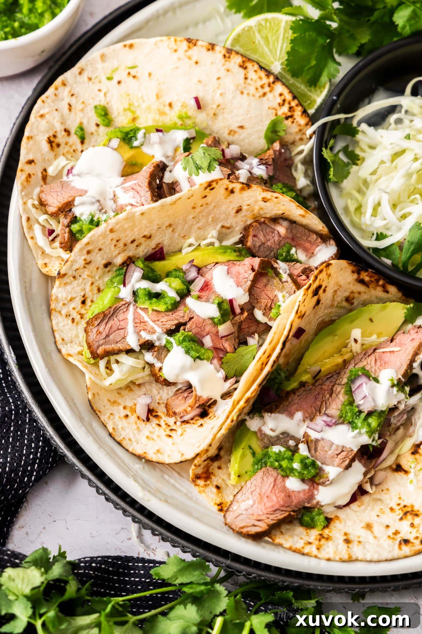 Closeup of 3 flank steak tacos on a plate.