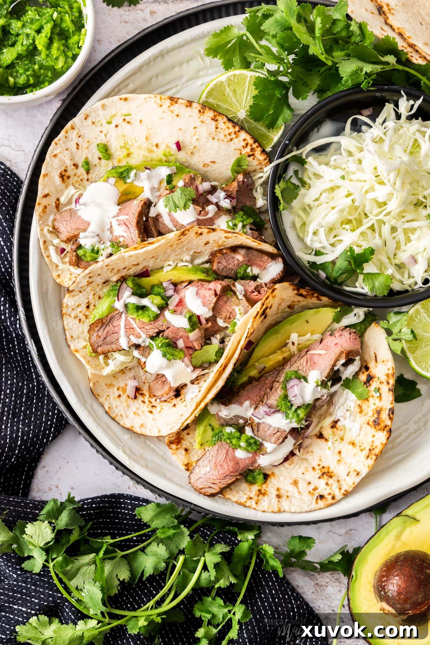 Top down view of 3 steak tacos on a plate surrounded by accompaniments.