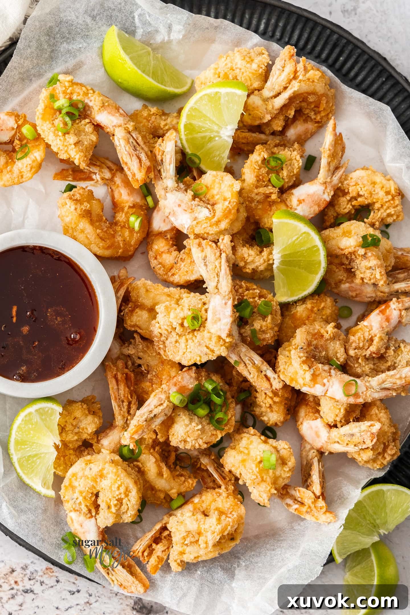 Top down view of a batch of crispy fried prawns on a tray with a bowl of hot honey for dipping.
