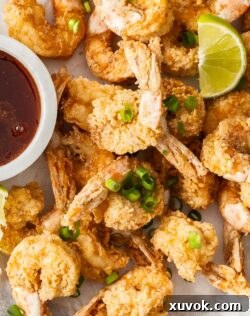 Top down view of crispy prawns topped with spring onions and wedges of lime.