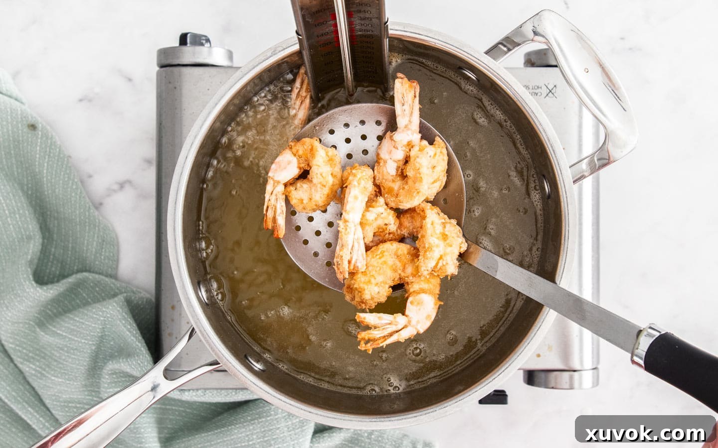 Fried prawns being scooped from hot oil with a slotted spoon after the first fry.