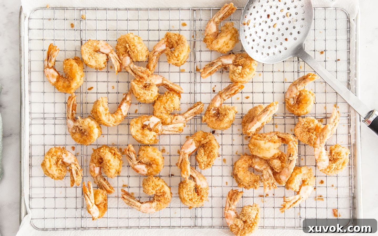 Crispy fried prawns resting on a wire rack after the second fry, perfectly golden.