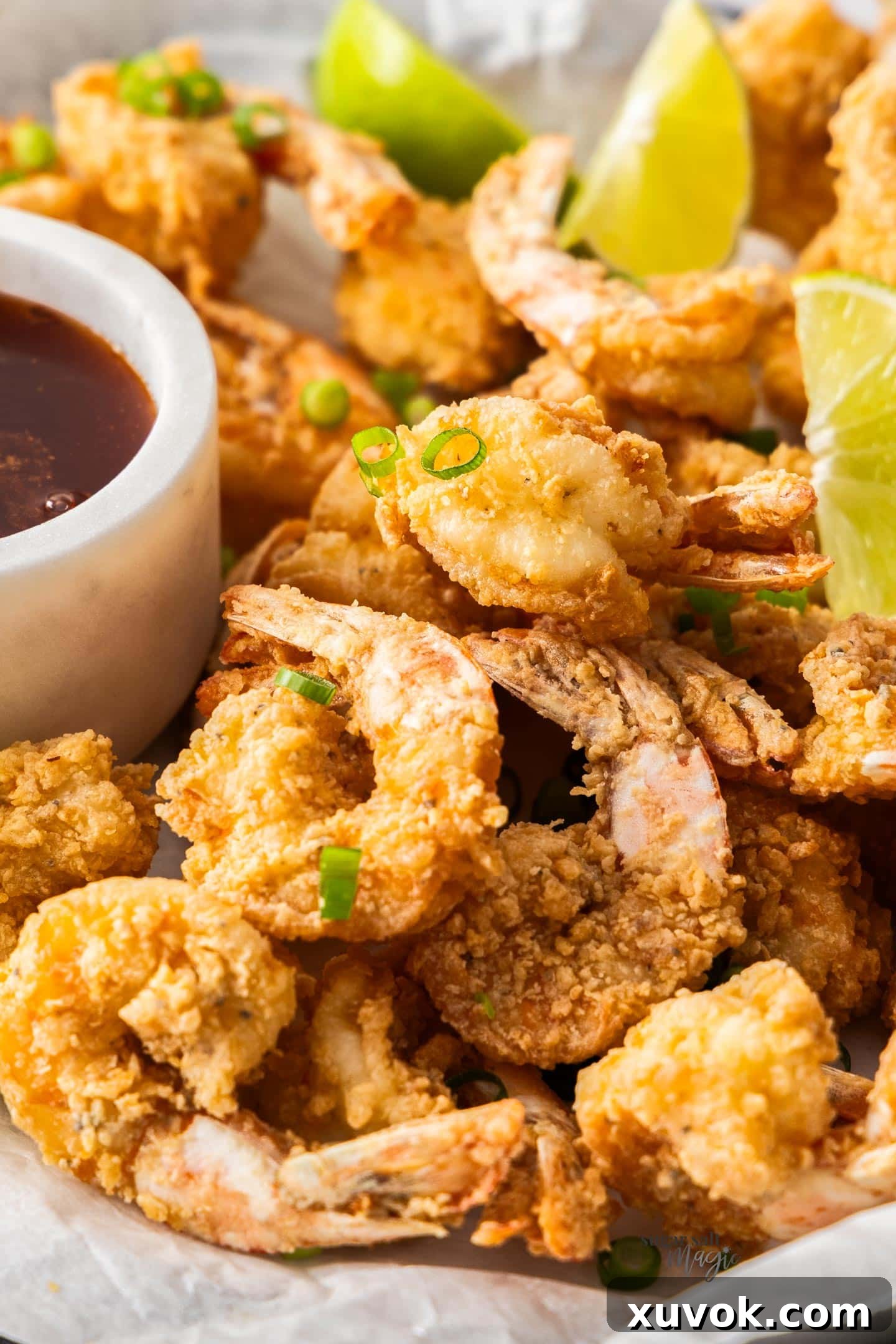 A pile of crispy prawns on a serving tray, garnished with lime wedges and fresh herbs.