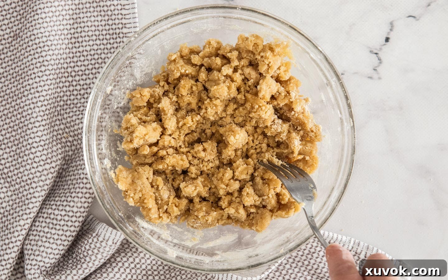 A fork mixing melted butter into the dry ingredients until clumping.