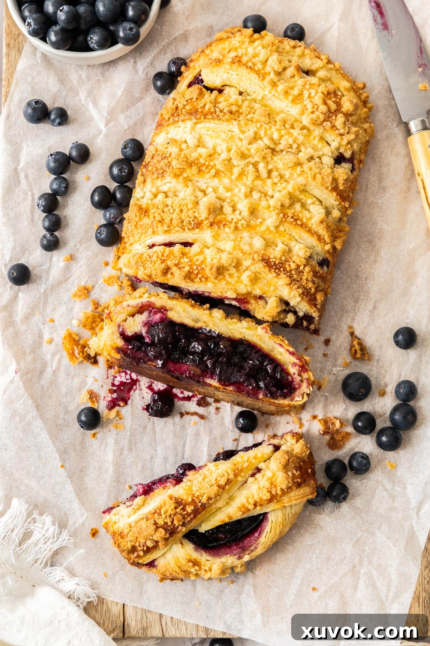 Top-down view of a golden-brown baked blueberry Danish braid with two slices cut away, revealing the vibrant blueberry filling and flaky layers. Perfect for a sweet breakfast or elegant brunch.