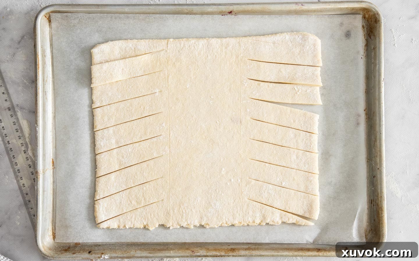 A piece of Danish dough rolled out, with strips precisely cut along the two side sections, ready for braiding.