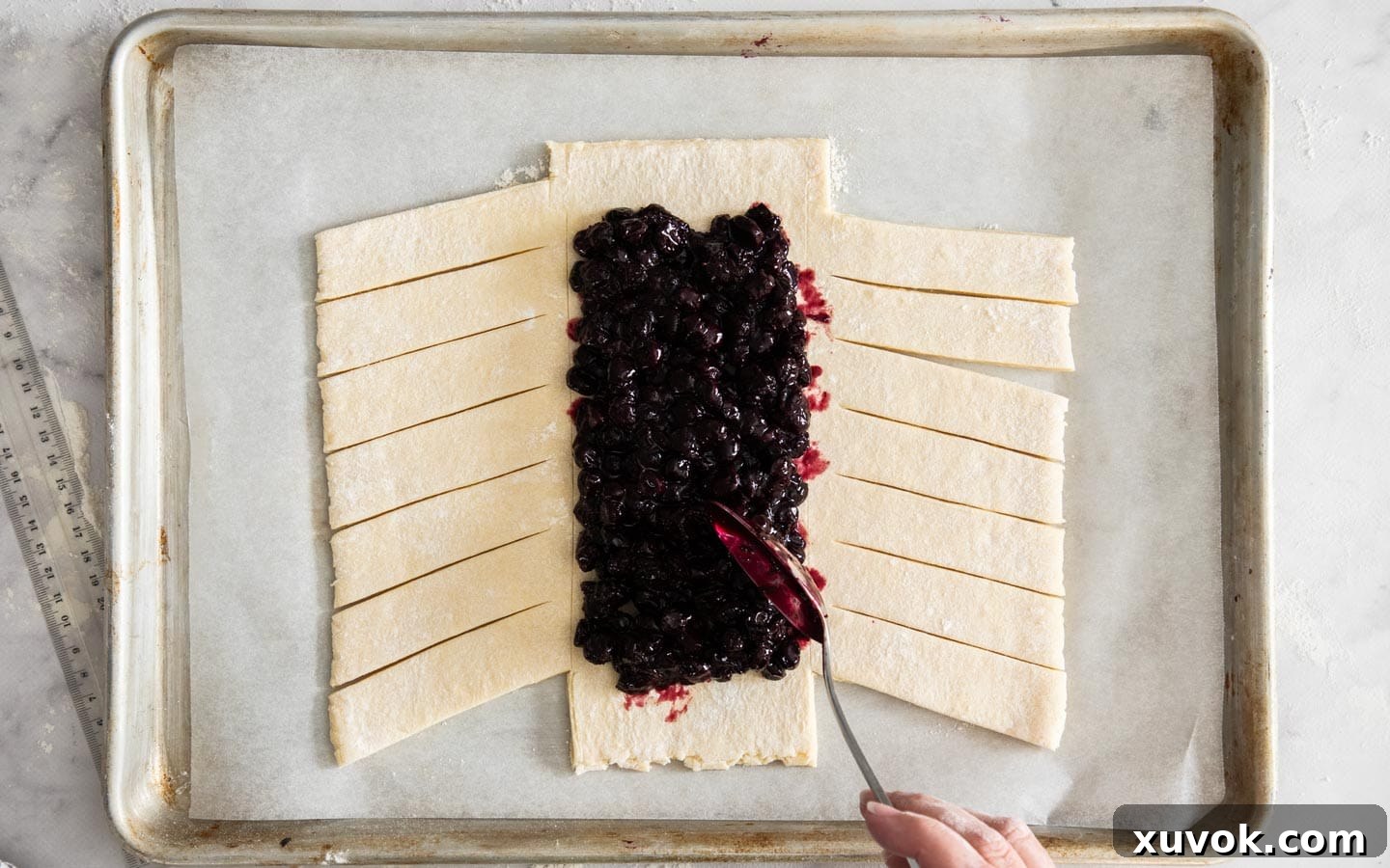 Adding the vibrant blueberry compote filling into the central section of the prepared Danish pastry dough.