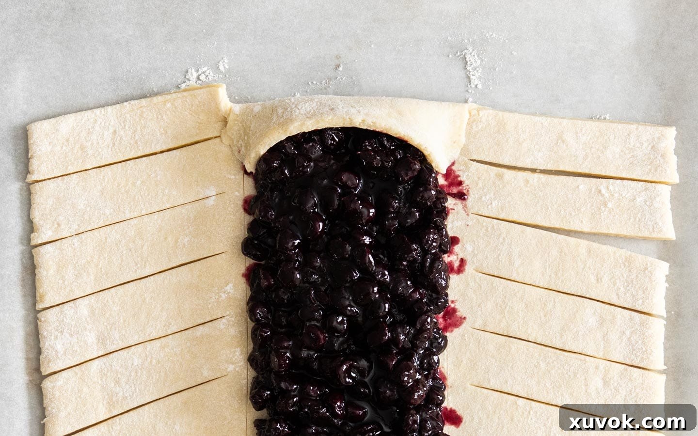 The top-middle portion of the Danish dough folded over the blueberry filling, securing the top edge.