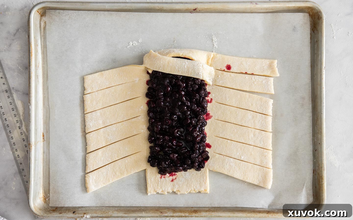 The first side strip of the Danish dough carefully pulled over the blueberry filling and secured, beginning the braid.