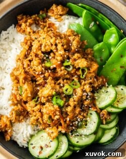Sticky chicken mince stir fry on top of a bowl of rice and greens, beautifully presented.