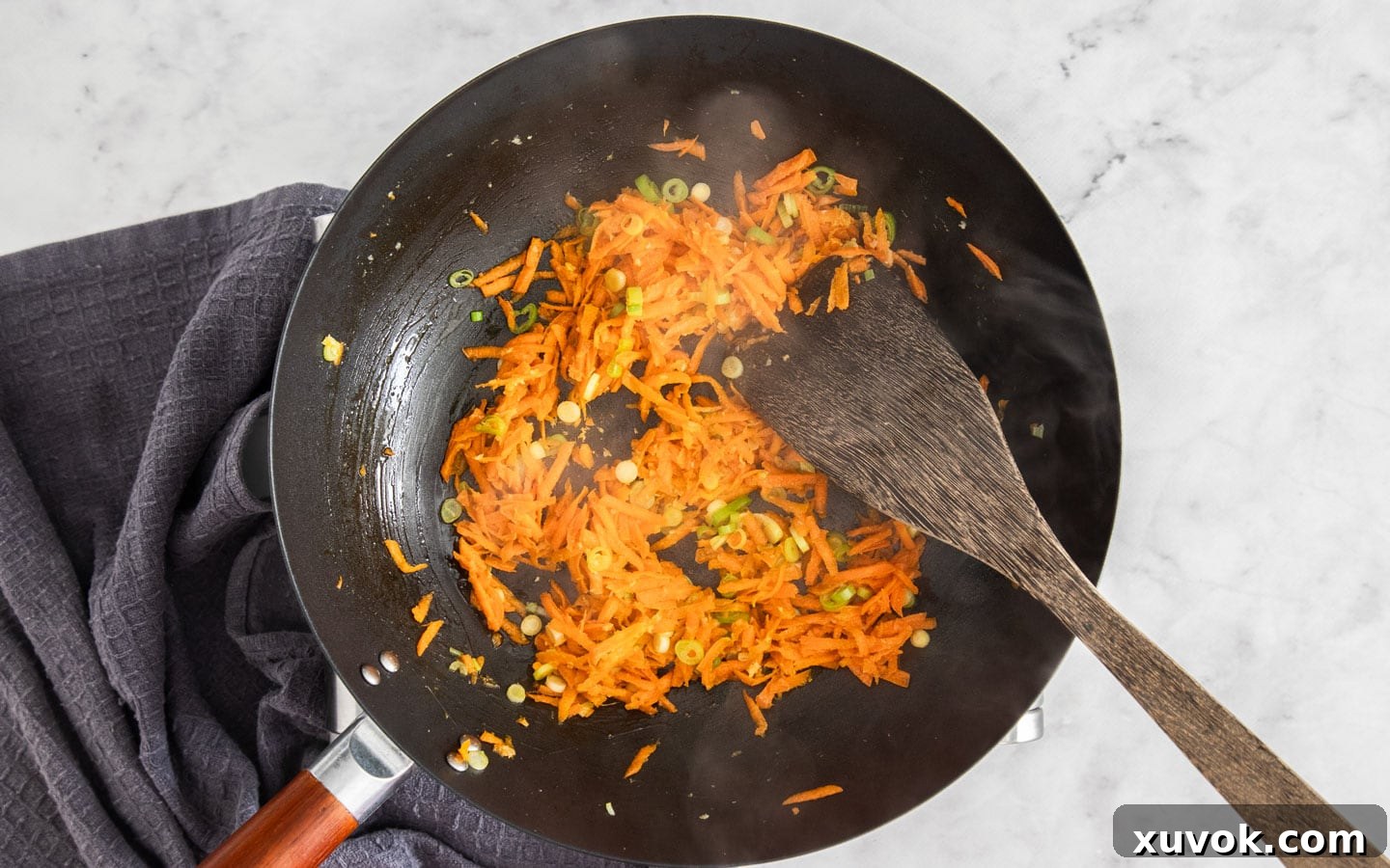 Finely grated carrot and aromatic ingredients gently softening in a hot wok, ready for the next step.