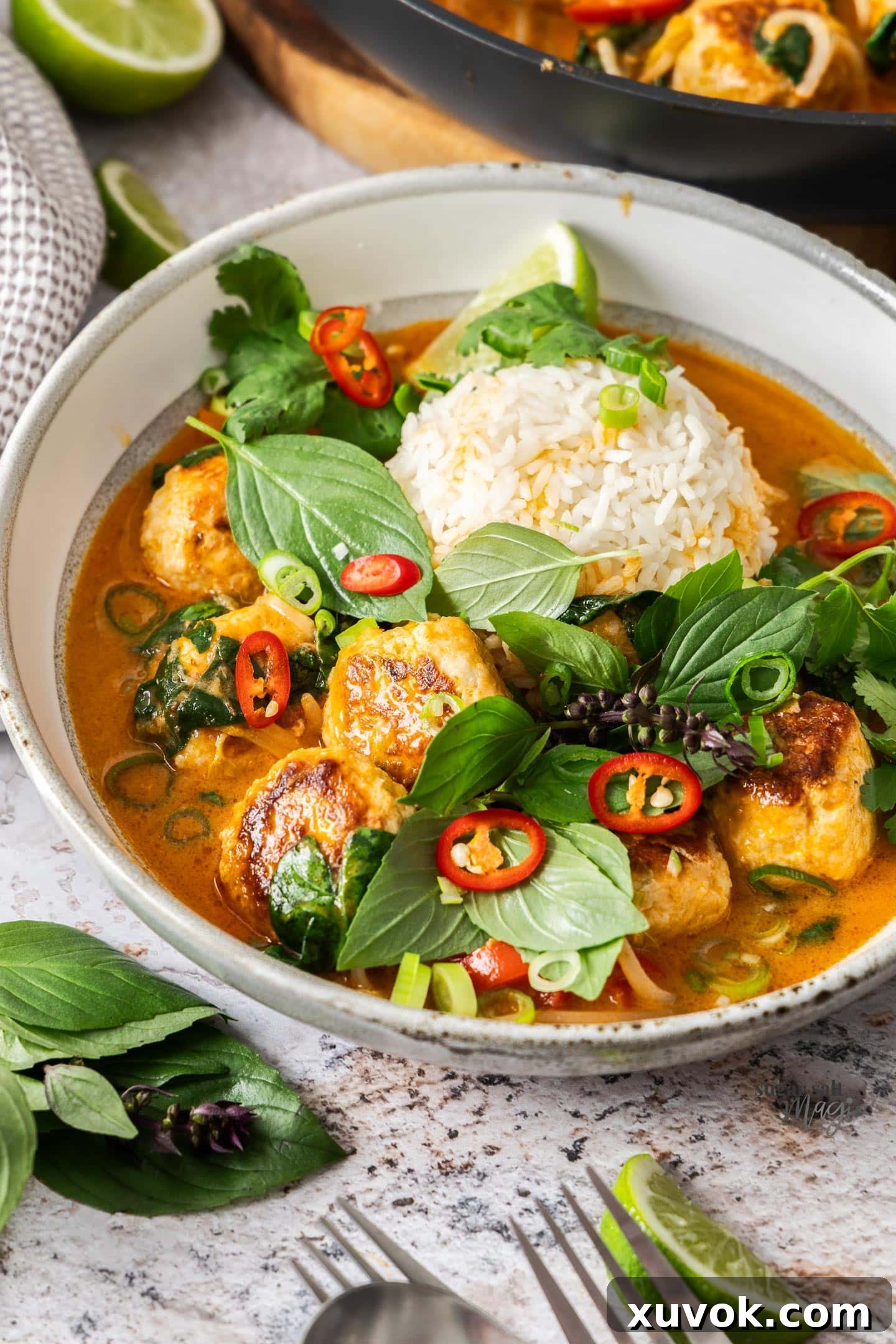 A dinner bowl filled with red curry meatballs, rice and topped with herbs.