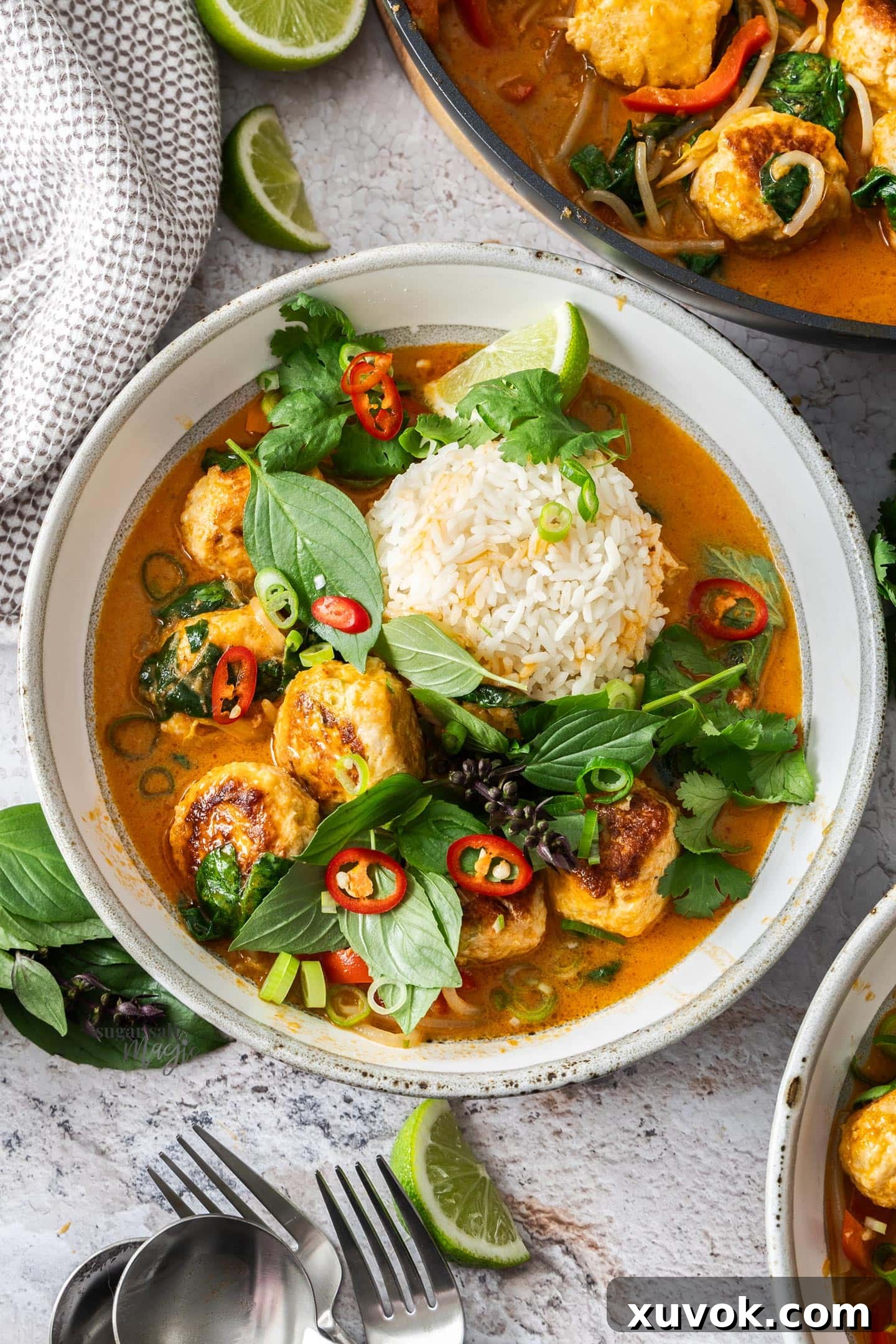 Top down view of red curry chicken meatballs in a dinner bowl with rice and herbs.