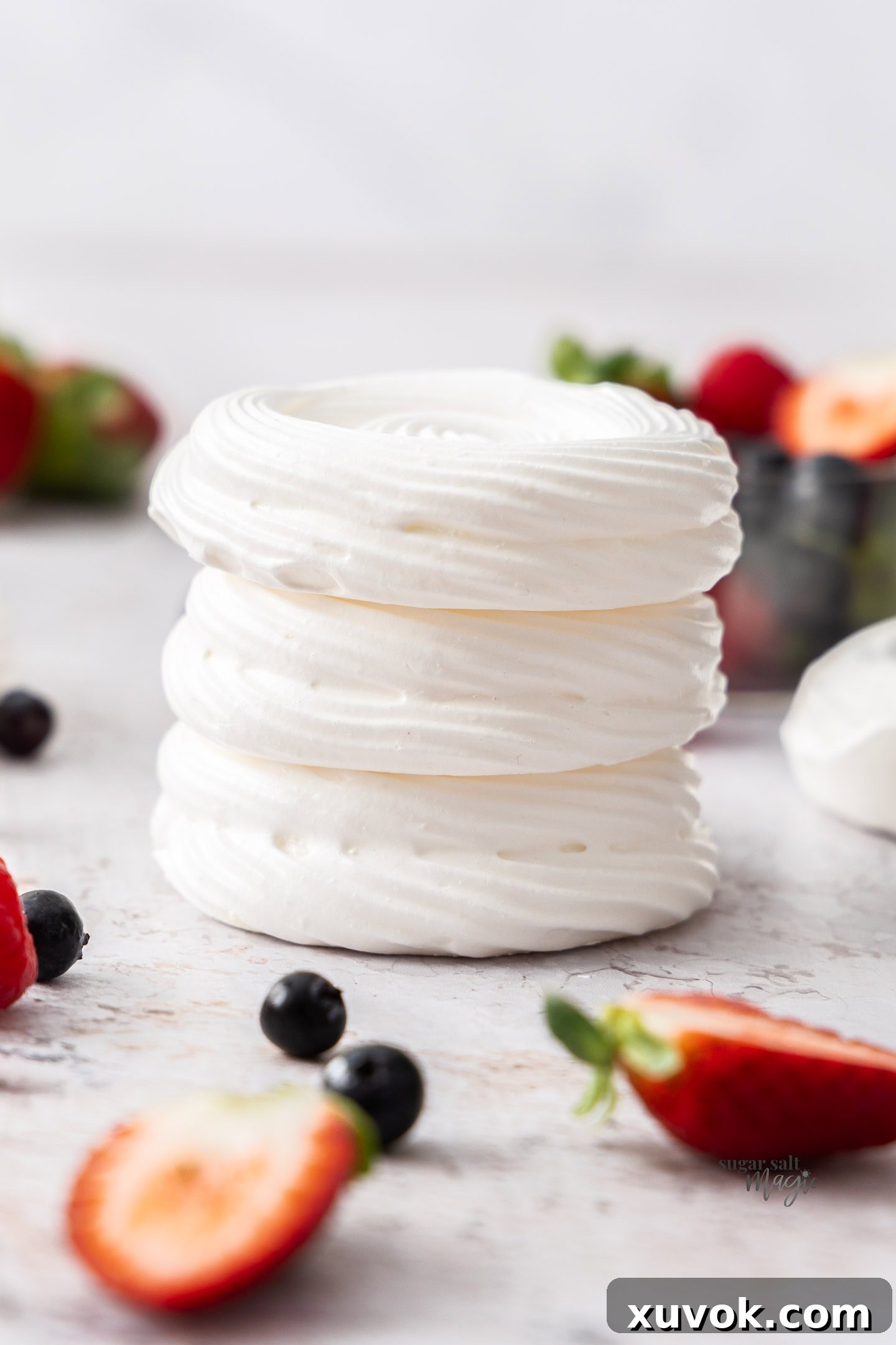 A stack of three perfectly formed meringue nests, artfully arranged and surrounded by an assortment of fresh berries, ready for serving or storage.