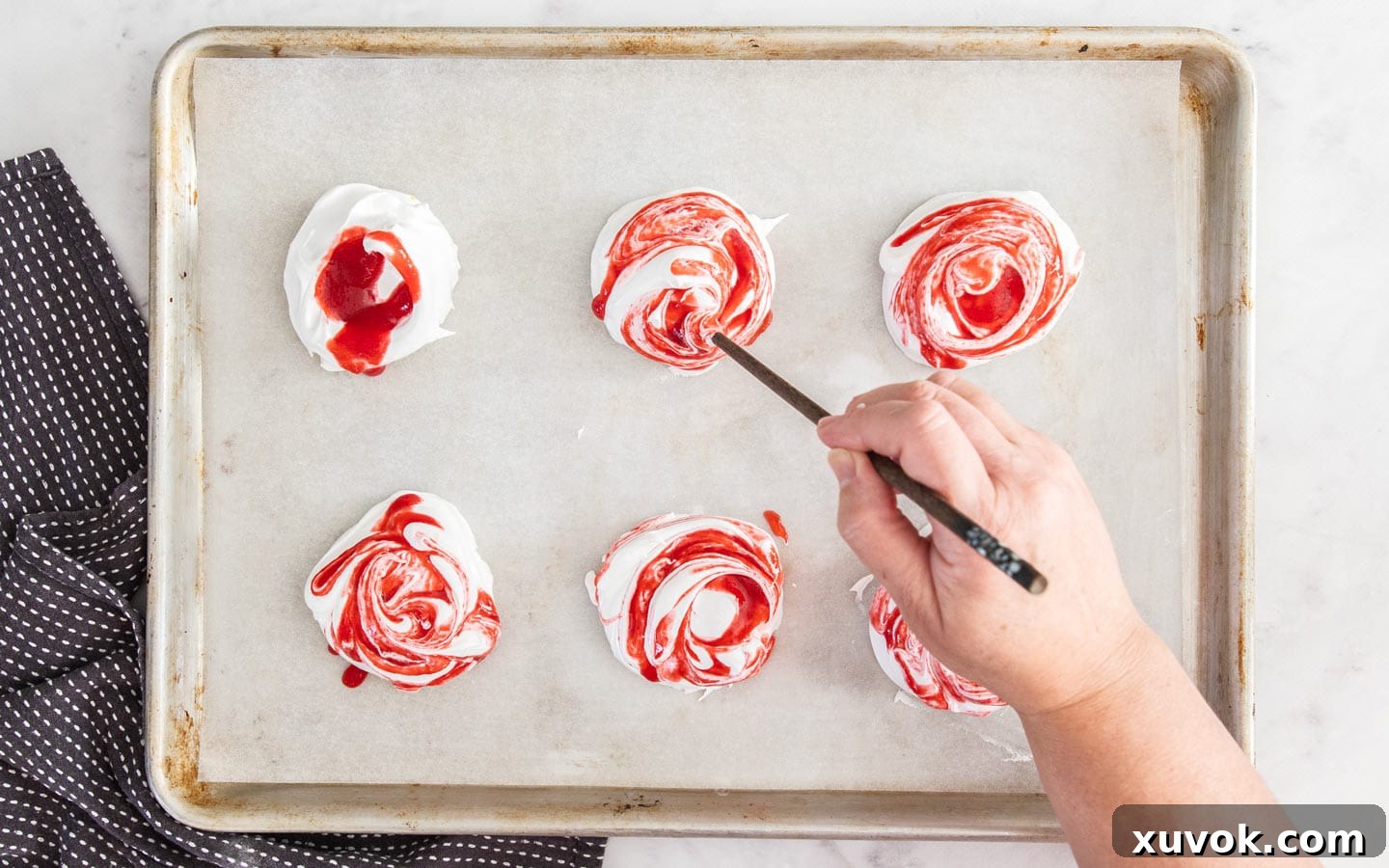 A chopstick gently swirling vibrant raspberry sauce through the pristine white meringue mixture.