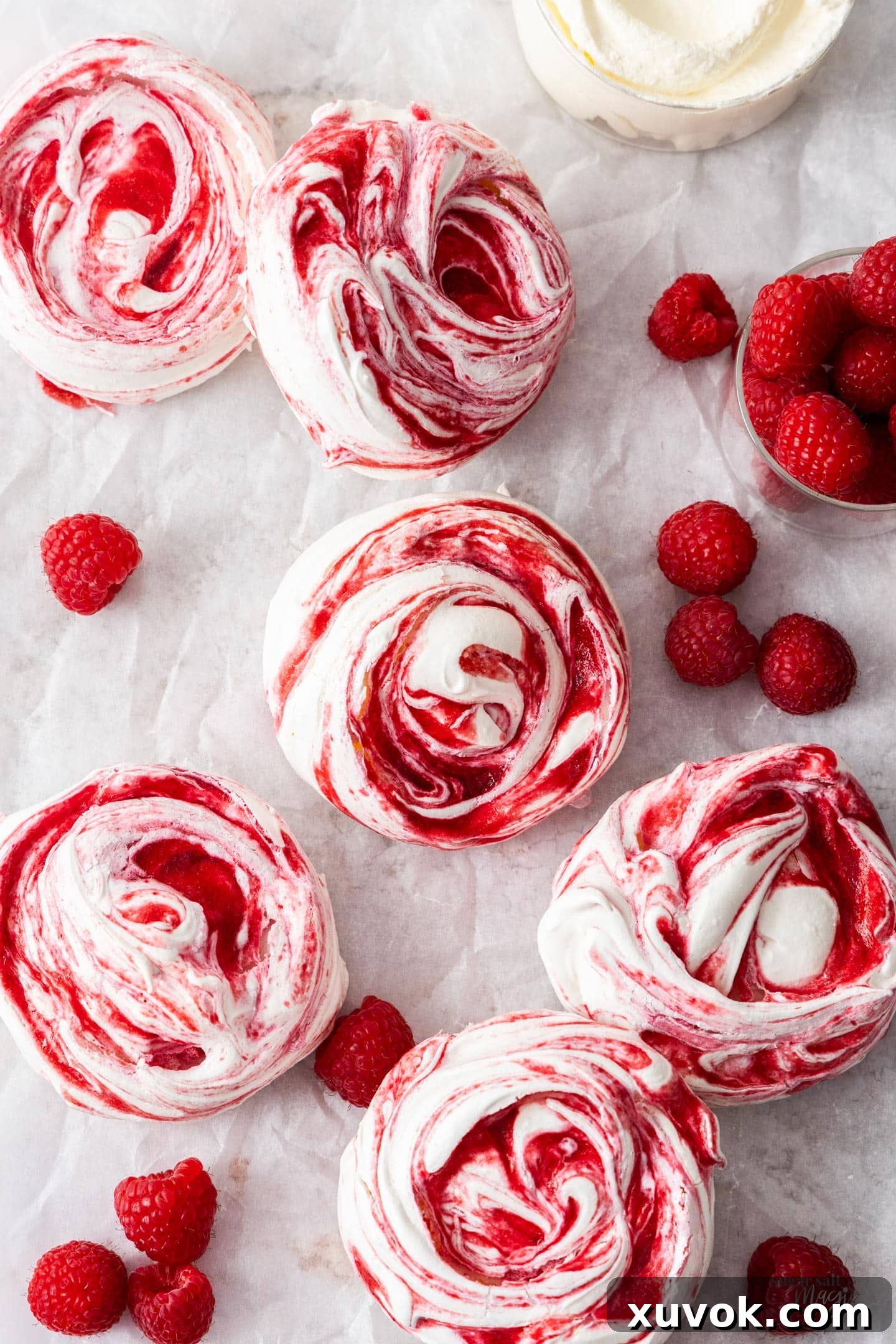 Top-down view of a batch of five perfectly swirled raspberry meringues on a baking sheet, freshly baked.