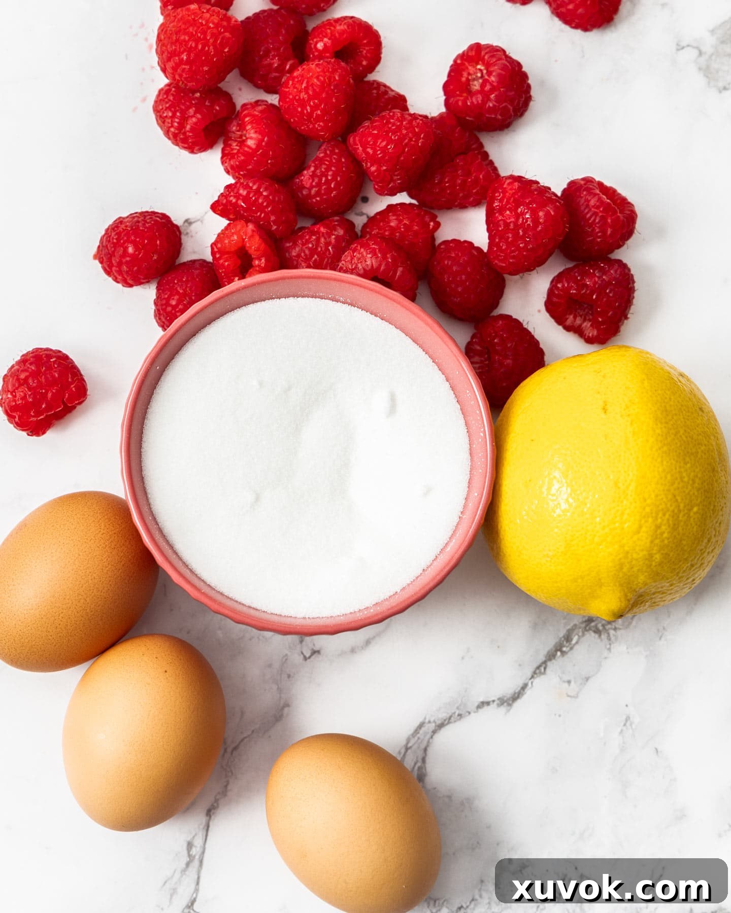 Ingredients for raspberry meringues laid out on an elegant marble surface, ready for preparation.