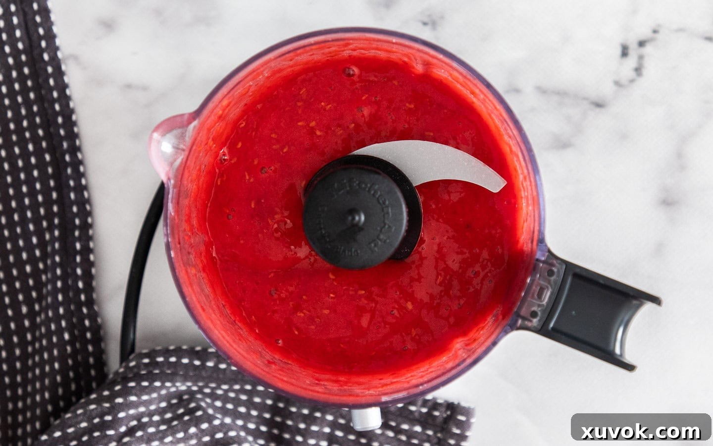 Raspberry sauce blending smoothly in a mini food processor, ready for straining.