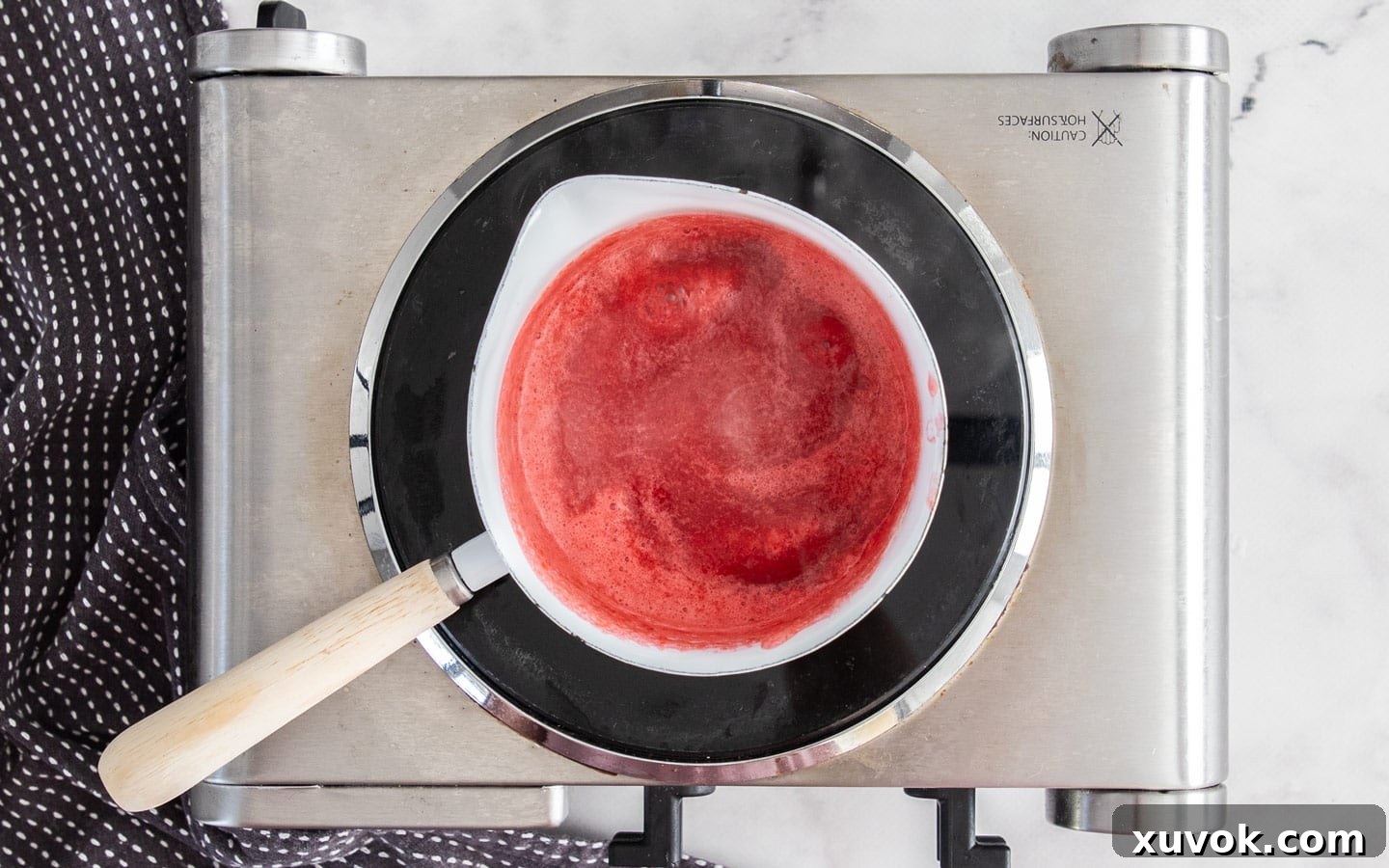 The raspberry sauce gently bubbling on the stove, visibly thickening as it reduces.