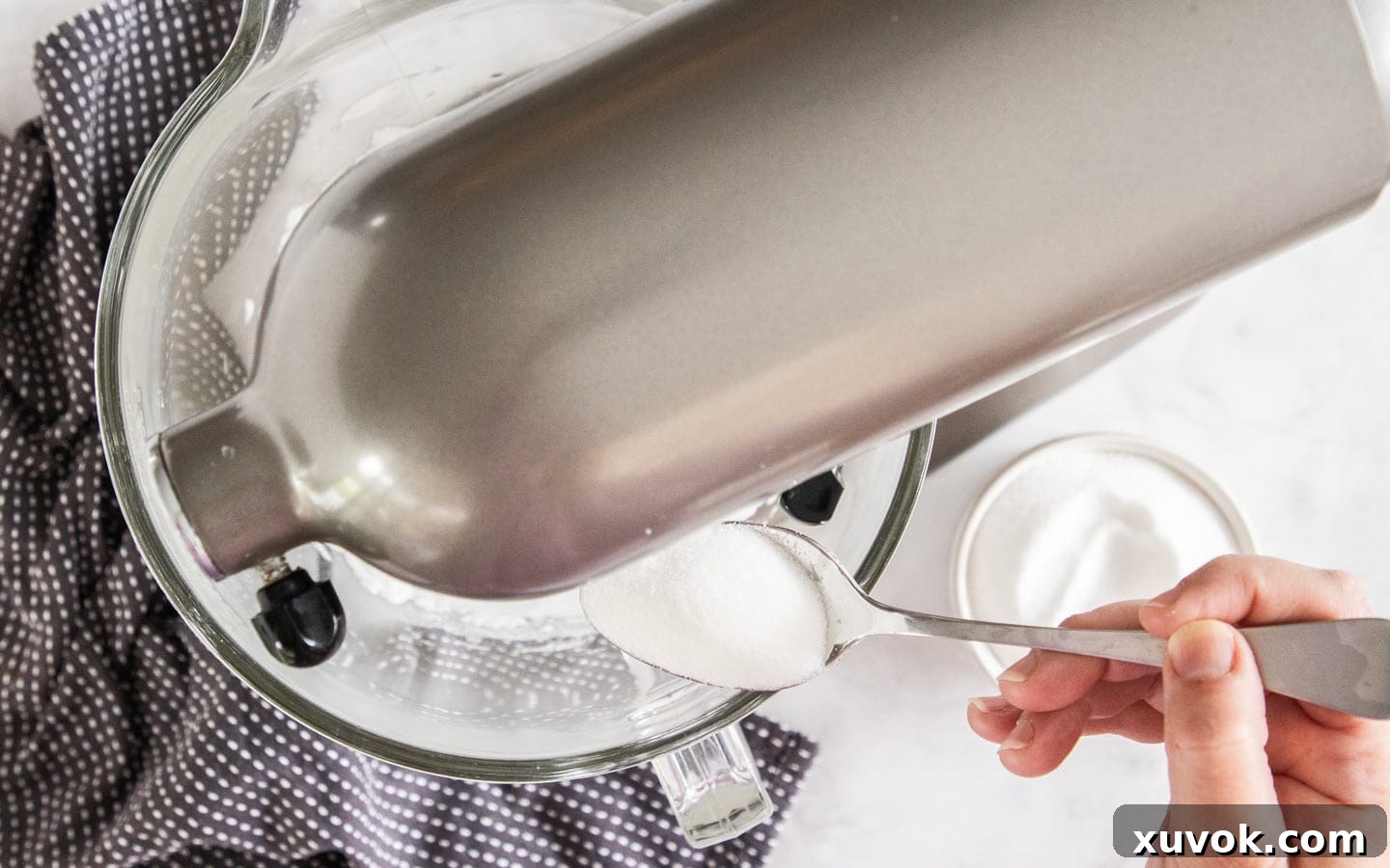 Granulated sugar being slowly added to the whipping meringue in a stand mixer.