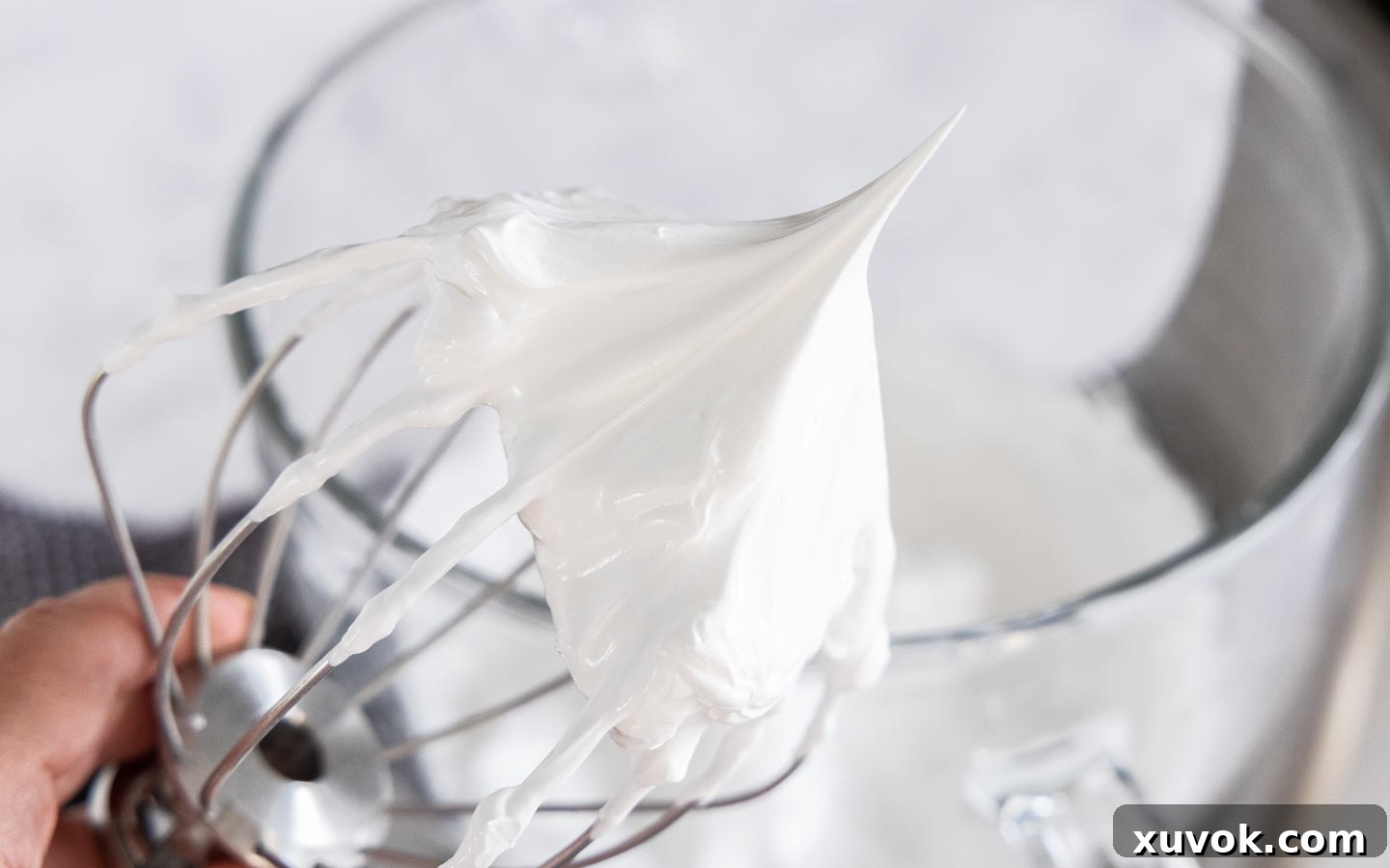 A whisk lifted from the meringue, showing a perfectly stiff peak standing firm and glossy.