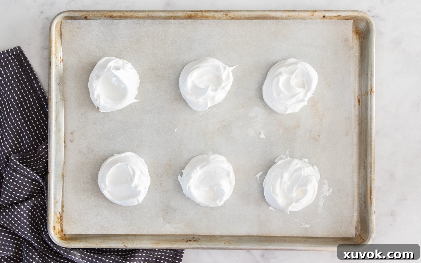 Six perfectly portioned mounds of meringue arranged on a baking sheet, ready for swirling with coulis.
