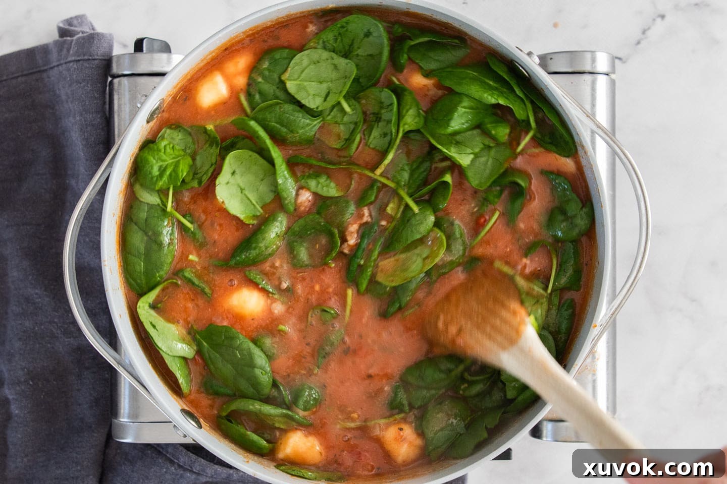 Fresh baby spinach being stirred into the steaming hot sausage gnocchi soup, adding color and nutrients just before serving.