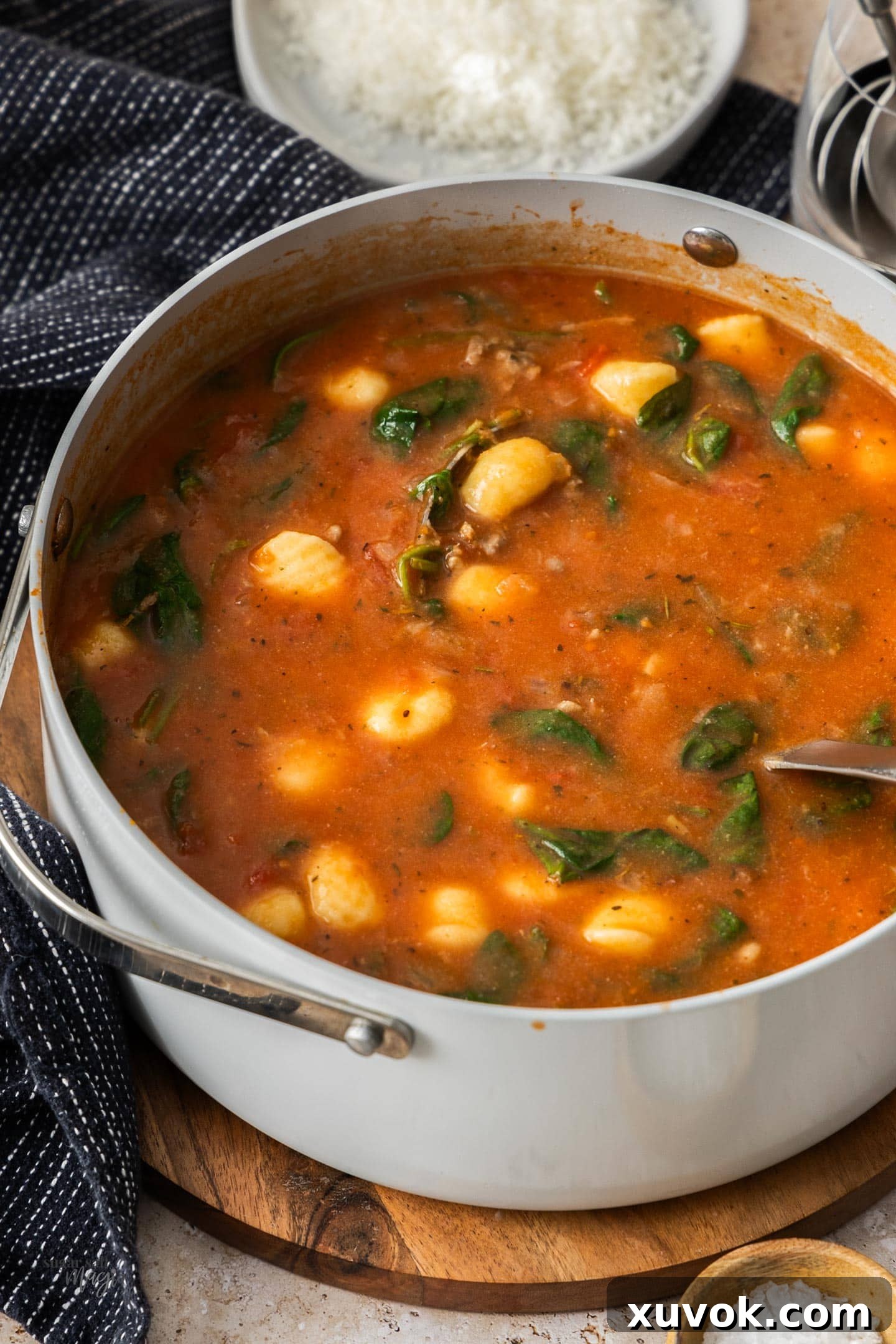 A large saucepan filled with steaming, rich gnocchi and sausage soup, sitting invitingly on a rustic wooden board.