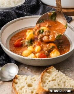 A ladle pouring steaming sausage gnocchi soup into a white bowl, ready to be served.