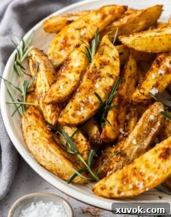 A platter piled up with crispy rosemary potato wedges with fresh rosemary leaves scattered around.