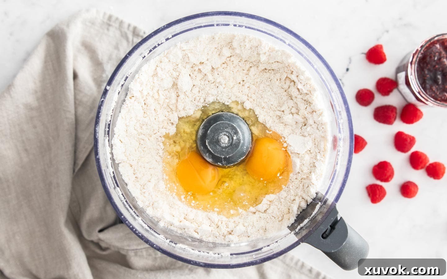 A food processor with the eggs on top of the flour mixture.