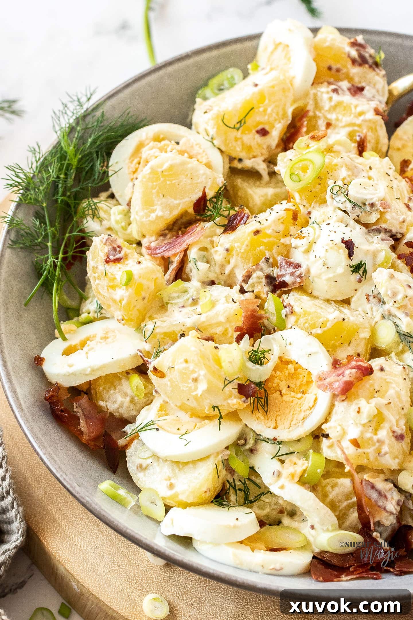 Closeup of a bowl full of potato salad with eggs, garnished with fresh herbs.