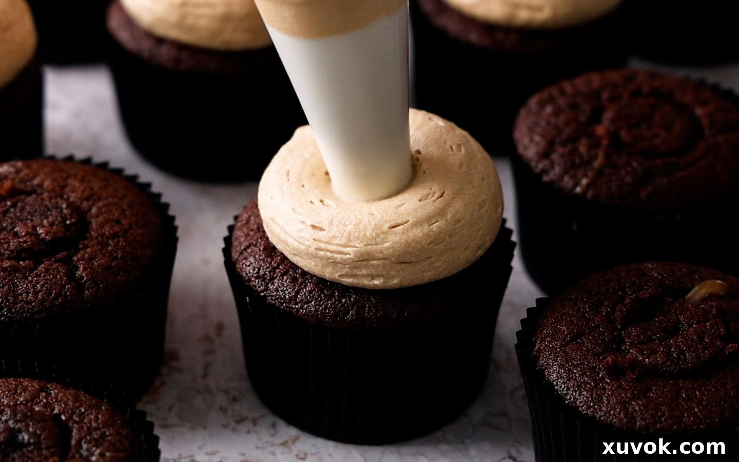 Caramel buttercream being expertly piped onto a chocolate cupcake, creating an elegant and tempting swirl.
