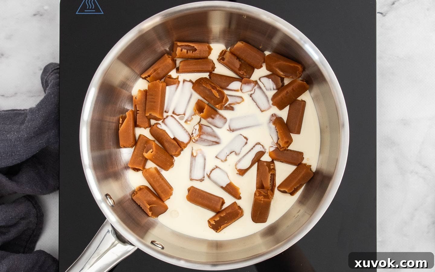 Unwrapped caramels and heavy cream gently heating in a saucepan, beginning to melt into a smooth sauce.
