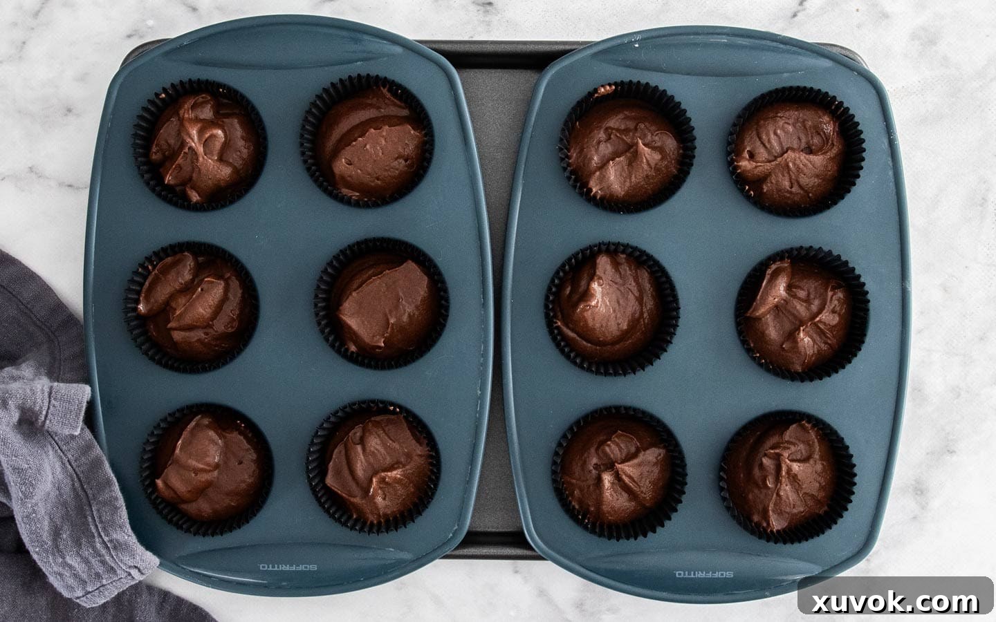 Chocolate cupcake batter neatly portioned into paper liners within a silicone muffin pan, ready for baking.