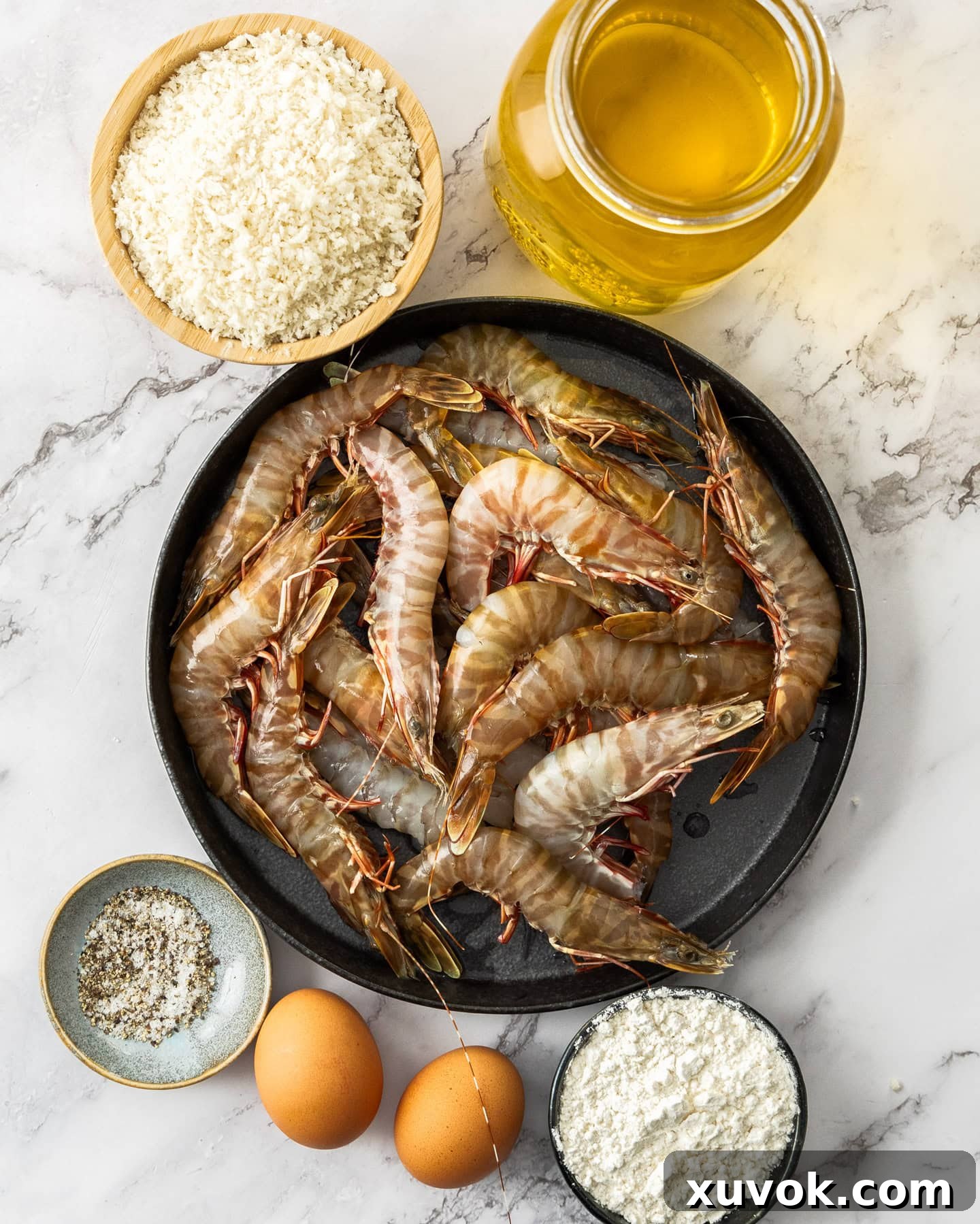 Ingredients for prawn katsu laid out on a marble surface, including prawns, panko, flour, eggs, and seasonings.