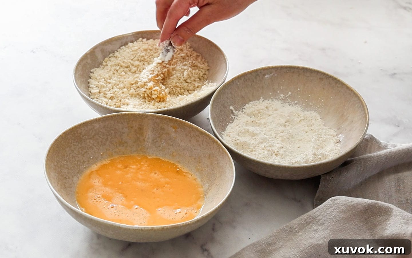 Three bowls for dredging the prawns; one with flour, one with egg wash, and one with panko breadcrumbs, ready for the breading process.
