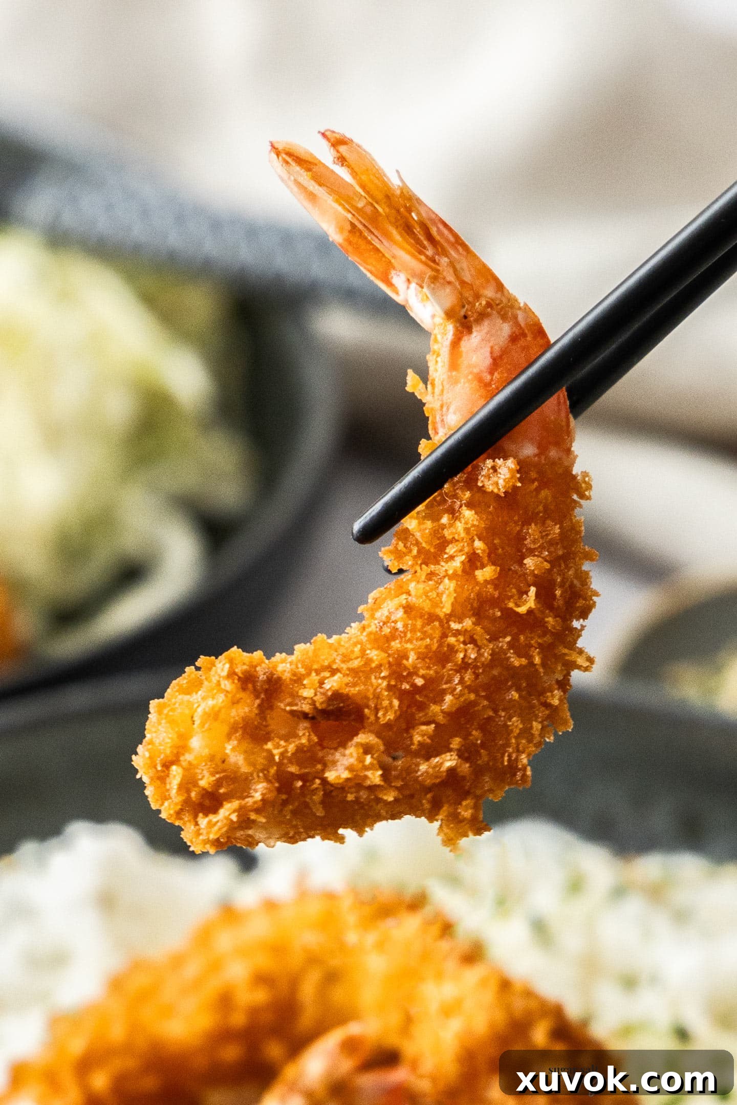 A closeup of chopsticks holding a panko fried prawn, highlighting its crunchy texture.